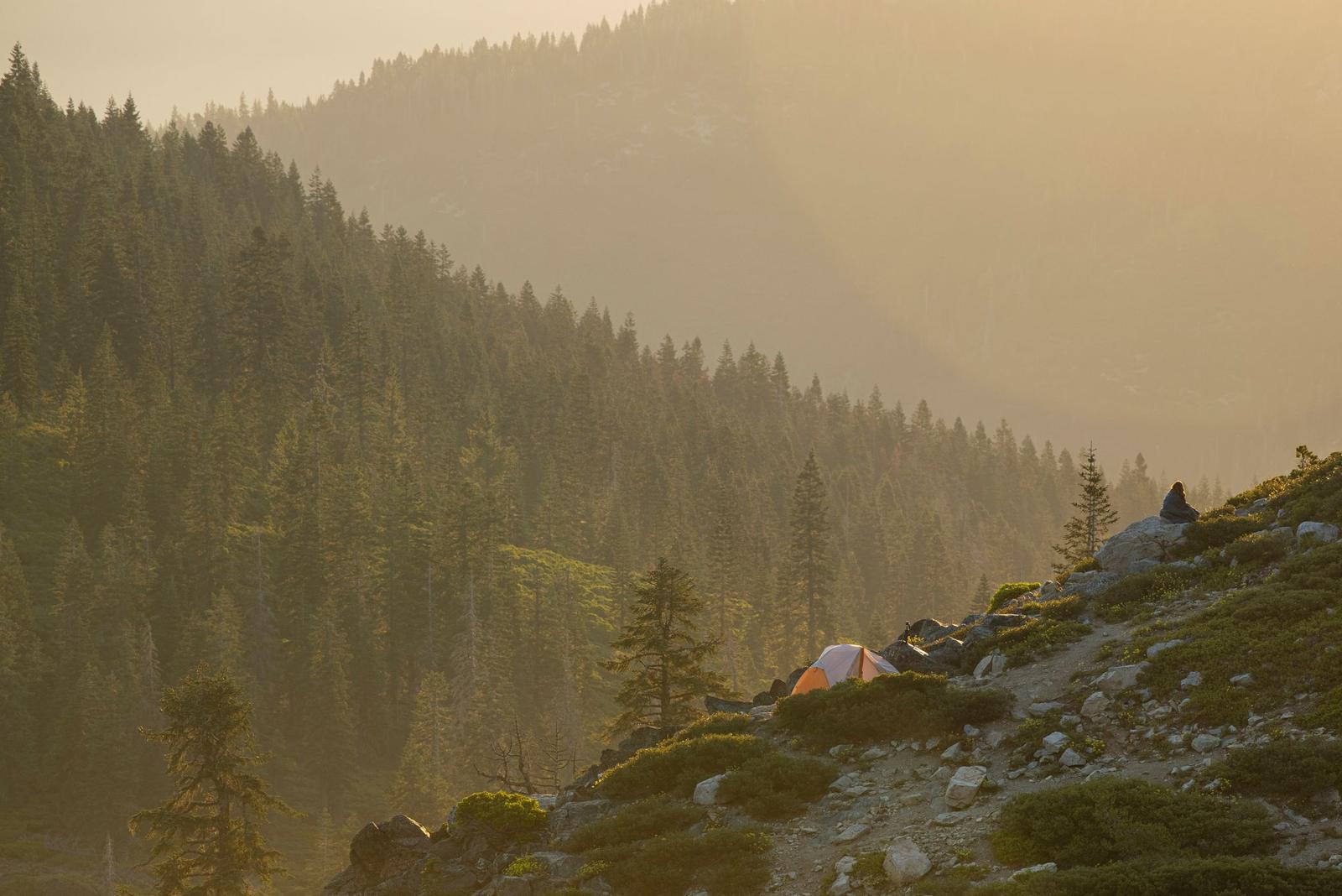 A tent catching the last light on a forested ridge
