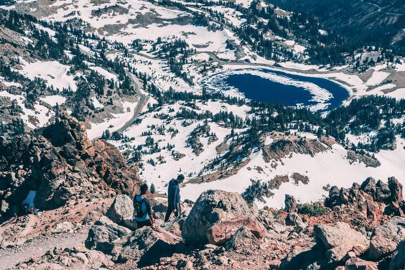 Hikers on a volcanic ridge above a snow-rimmed lake