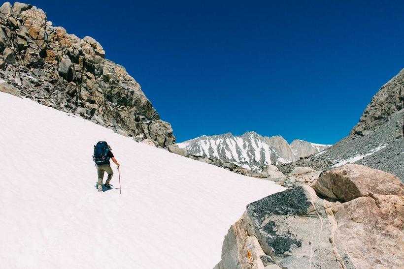 A mountaineer crossing a snowfield below a rocky summit